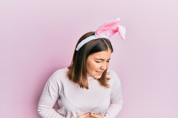 Sticker - Young beautiful woman wearing cute easter bunny ears with hand on stomach because nausea, painful disease feeling unwell. ache concept.