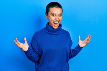 Poster - Beautiful hispanic woman with short hair wearing turtleneck sweater crazy and mad shouting and yelling with aggressive expression and arms raised. frustration concept.