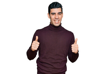 Handsome hispanic man wearing casual turtleneck sweater success sign doing positive gesture with hand, thumbs up smiling and happy. cheerful expression and winner gesture.