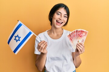 Poster - Young caucasian woman holding israel flag and shekels banknotes smiling and laughing hard out loud because funny crazy joke.