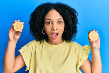 Sticker - Young african american girl holding lemon afraid and shocked with surprise and amazed expression, fear and excited face.