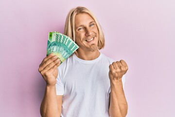 Canvas Print - Caucasian young man with long hair holding 20000 indonesian rupiah screaming proud, celebrating victory and success very excited with raised arm