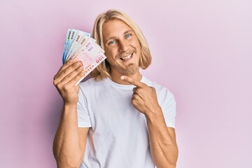 Sticker - Caucasian young man with long hair holding new taiwan dollars banknotes smiling happy pointing with hand and finger