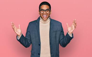 Young handsome hispanic man wearing business jacket and glasses celebrating victory with happy smile and winner expression with raised hands