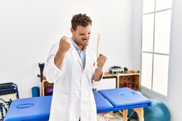 Sticker - Handsome young man working at pain recovery clinic very happy and excited doing winner gesture with arms raised, smiling and screaming for success. celebration concept.