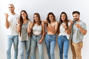 Group of young friends standing together over isolated background cheerful with a smile on face pointing with hand and finger up to the side with happy and natural expression