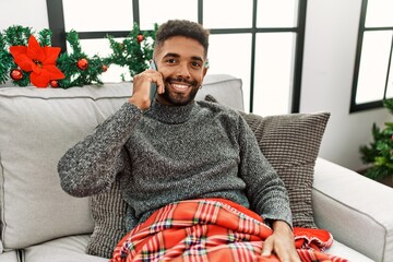 Wall Mural - Young african american man smiling happy talking on the smartphone celebrating christmas at home.