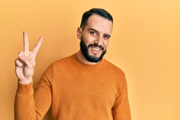 Young man with beard wearing casual winter sweater showing and pointing up with fingers number two while smiling confident and happy.