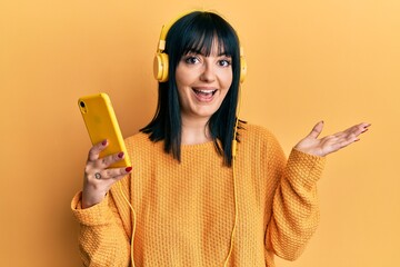 Sticker - Young hispanic woman using smartphone wearing headphones celebrating achievement with happy smile and winner expression with raised hand