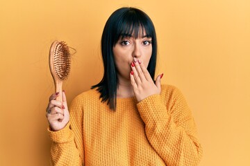 Sticker - Young hispanic woman holding comb loosing hair covering mouth with hand, shocked and afraid for mistake. surprised expression