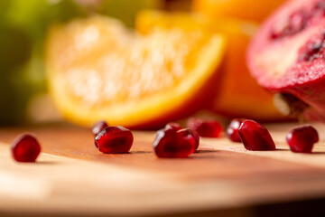 Sticker - Closeup of pomegranate seeds on a wooden cutting board with other fruits in the blurry background