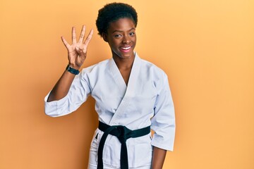 Canvas Print - Young african american girl wearing karate kimono and black belt showing and pointing up with fingers number four while smiling confident and happy.