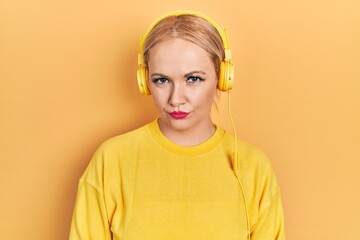 Canvas Print - Young blonde woman listening to music using headphones skeptic and nervous, frowning upset because of problem. negative person.