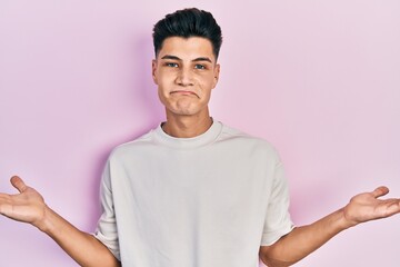 Canvas Print - Young hispanic man wearing casual white t shirt clueless and confused with open arms, no idea and doubtful face.