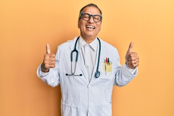 Wall Mural - Middle age indian man wearing doctor coat and stethoscope success sign doing positive gesture with hand, thumbs up smiling and happy. cheerful expression and winner gesture.