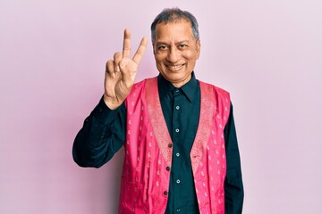 Canvas Print - Middle age indian man wearing traditional indian clothes showing and pointing up with fingers number two while smiling confident and happy.