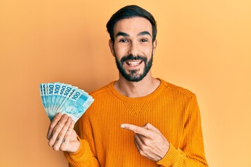 Wall Mural - Young hispanic man holding 100 brazilian real banknotes smiling happy pointing with hand and finger