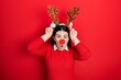 Young hispanic woman wearing deer christmas hat and red nose doing funny gesture with finger over head as bull horns