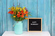Happy Wednesday words on black letter board and bouquet of bright wildflowers in tin can vase on table against blue wooden wall. Concept Hello Wednesday