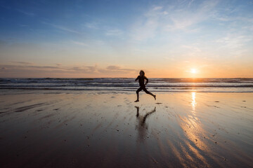 Wall Mural - young girl running and jumping with happiness on the beach at sunset