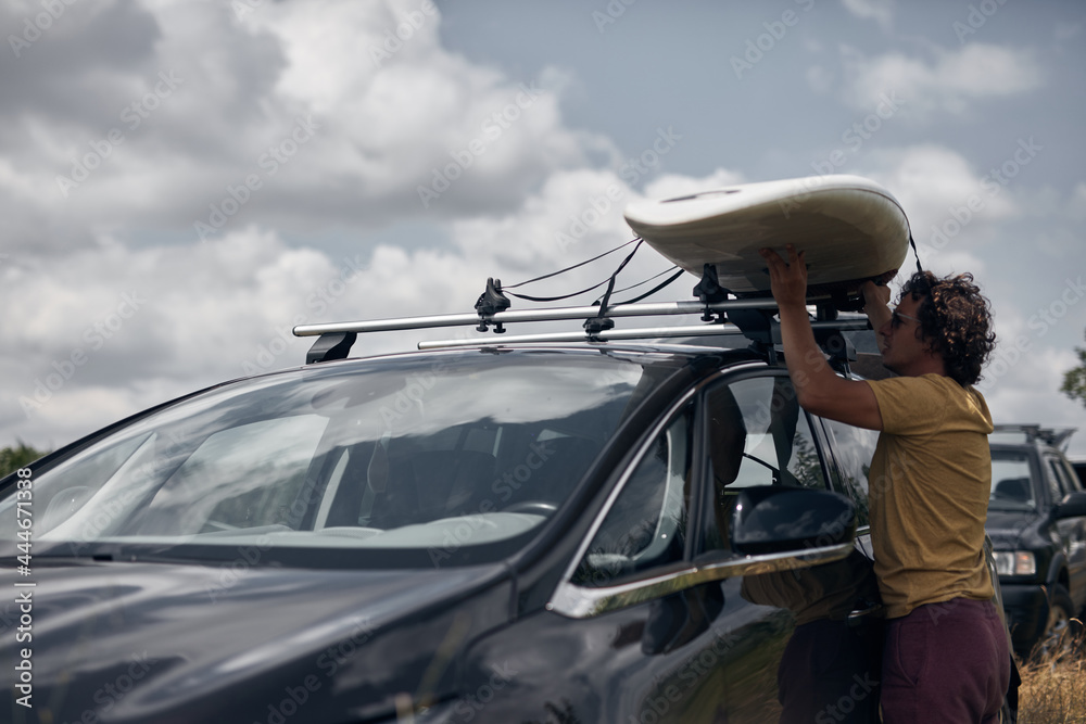 Windsurfer and camper packing and unpacking from a car's roof rack in ...