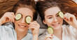 © Daria Lukoiko - Two girls make homemade face and hair beauty masks. Cucumbers for the freshness of the skin around the eyes. Women take care of youthful skin. Girlfriends laugh at home lying on the floor on pillows.