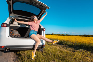 Wall Mural - smiling pretty woman sitting in suv car trunk on sunset looking at farm field