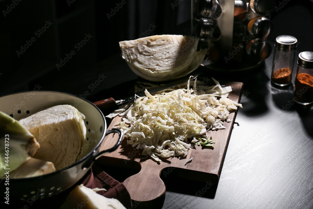 Board with fresh chopped cabbage on dark wooden table
