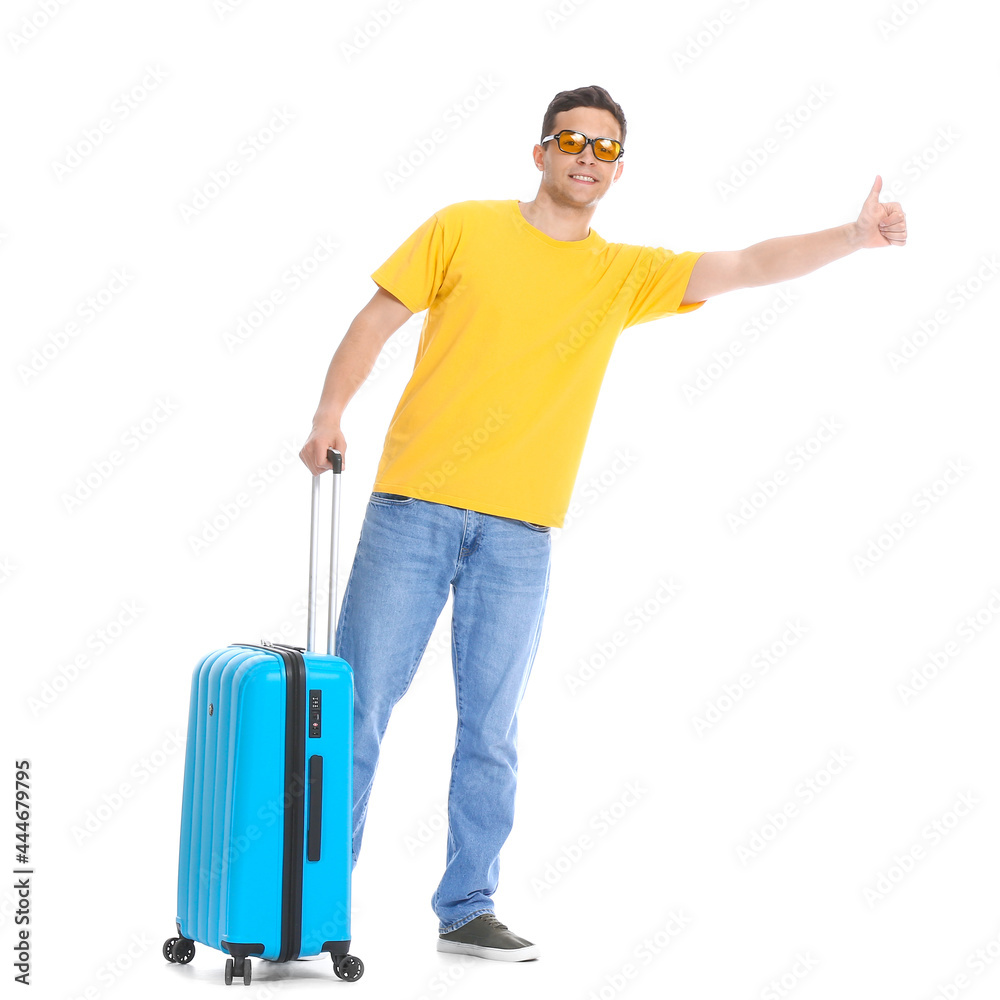 Young man with suitcase hitchhiking on white background
