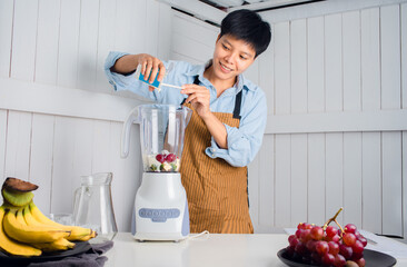 Smiling Asian man  prepared to Make blending, Smoothie fruit vegetables with Swiss Chard, banana, and red grape  at a white kitchen home. people are taking care of themselves.