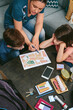 © David Pereiras - Top view of mother explaining to her children the assembly point map while preparing emergency backpacks