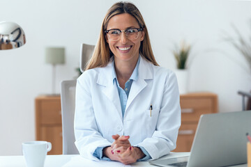 Mature attractive female doctor looking at camera while working sitting in the consultation.