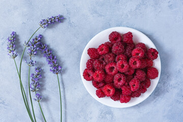 Raspberry plate lavender on a gray table top view. Ripe raspberries in close-up. The concept of summer food, freshness, vitamins. Beautiful berries on a gray background. Summer dietary healthy dessert