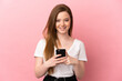 © luismolinero - Teenager girl over isolated pink background looking at the camera and smiling while using the mobile