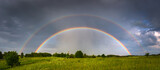 Fototapeta Tęcza - Rainbow over stormy sky. Rural landscape with rainbow over dark stormy sky in a countryside at summer day.