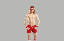 Funny Topless Skinny Man In Glasses, Red Retro Sweatband And Shorts Standing Isolated On Gray Background, Grinning, Winking Eye And Showing His Weak Thin Body After First Ever Sports Exercise Workout