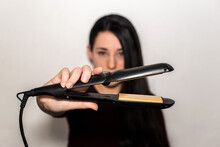 Pretty Young Woman With Dark Long Hair Holding A Flat Iron In One Hand. Hair Straightener