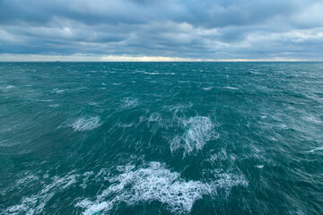 Heavy storm in the ocean. Big waves in the open sea, cloudy sky during a storm and a cargo ship on the horizon.