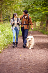 Couple With Pet Golden Retriever Dog Hiking Along Path Through Trees In Countryside