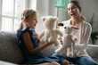 © fizkes - Playful happy young Caucasian mom and small teen daughter have fun play puppet theatre at home. Smiling mother and little girl child engaged in playful game activity with teddy bear toys together.
