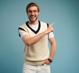 Sticker - Portrait of a happy young man in casual pointing fingers away at copy space isolated over blue background.