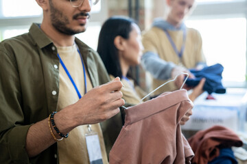 Wall Mural - Young man and other people choosing free clothes in volunteering office