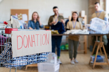 Wall Mural - Shopping cart with donation clothes against row of volunteers standing by table