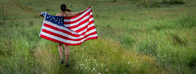 Back view of a girl with an American flag in a field among the grass.