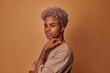 © antianti - Lovely blonde African American woman keeps hand on face has gentle smile looks satisfied at camera poses against beige background. Cute glad mixed race female indoor