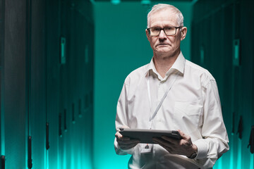 Wall Mural - Waist up portrait of senior data scientist looking at camera and holding tablet while working with supercomputer in futuristic blue light, copy space