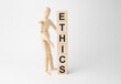 Wooden mannequin near tower of cubes with word ethics on table against light background