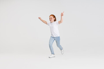 Wall Mural - Beautiful cute little red-headed girl in casual outfit running. playing isolated on white studio background. Happy childhood concept. Sunny child