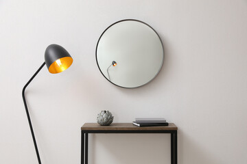 Console table and lamp near light wall with mirror indoors. Interior design