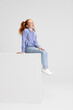 canvas print picture - One cute red-headed girl in casual clothes sitting on big box isolated on white studio background. Happy childhood concept. Sunny child. Looks happy, delighted